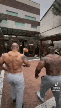 two muscular men are standing next to each other on a sidewalk in front of a building .
