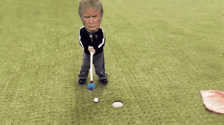 a doll with donald trump 's head on it is laying on a golf course