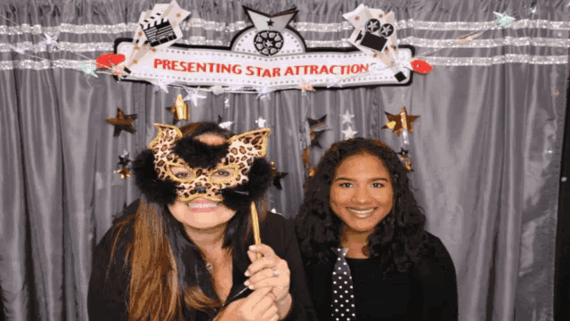 two women pose for a photo in front of a sign that says presenting star attraction