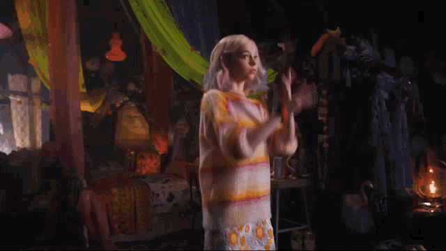 a woman in a striped sweater stands in a dark room with her arms in the air