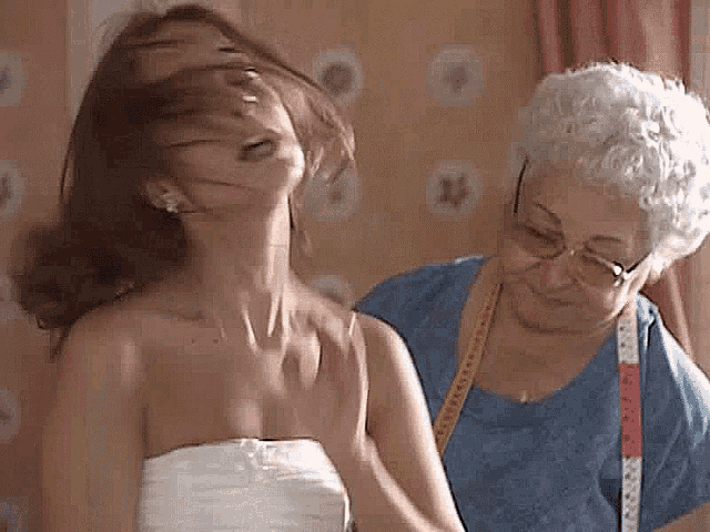 a woman in a white dress is being measured by an older woman with glasses