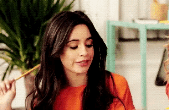a woman in an orange shirt is holding a pencil in her hand .