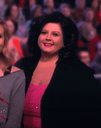 a woman in a pink dress and black jacket is smiling in front of a crowd