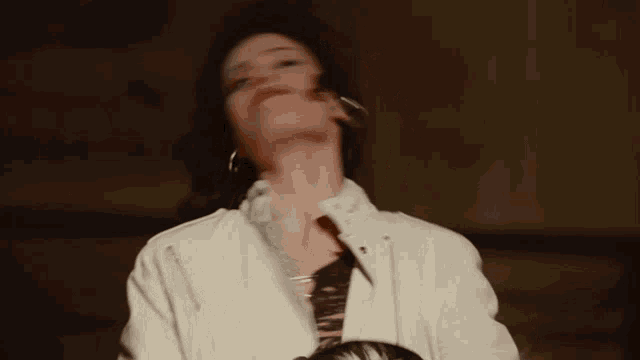 a woman in a white jacket is singing into a microphone with her eyes closed