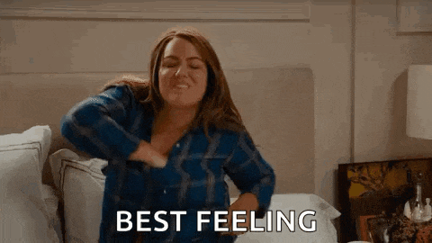 a woman is sitting on a bed with her hands on her chest and the words `` best feeling '' written on the screen .