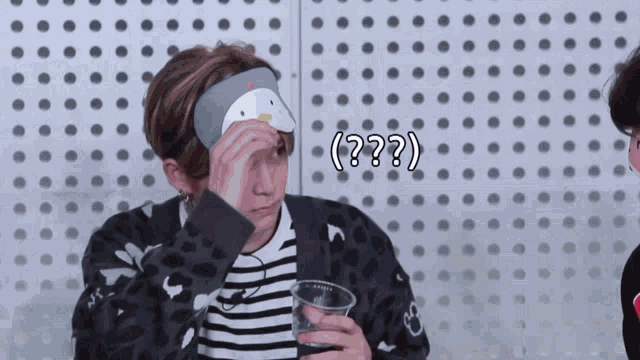 a man wearing a headband with a penguin on it is holding a cup and covering his eyes with his hand