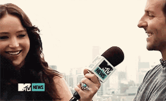 a woman is smiling while being interviewed by a man with a mtv news microphone