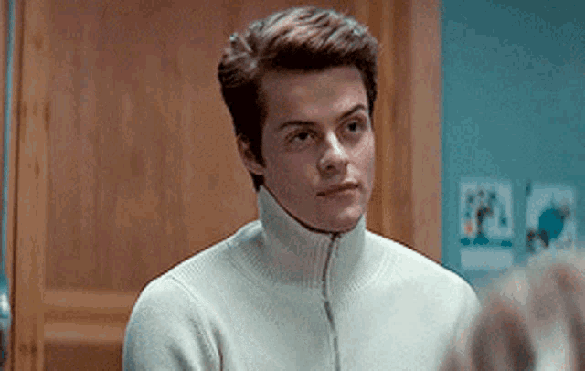 a young man wearing a white sweater is looking at himself in a mirror .