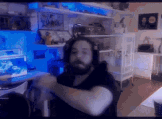 a man with a beard is sitting in front of a computer in a room with a fish tank in the background .