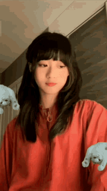 a woman in a red shirt is holding her hands up in front of her face