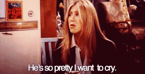 a woman is sitting in front of a refrigerator and saying he 's so pretty i want to cry