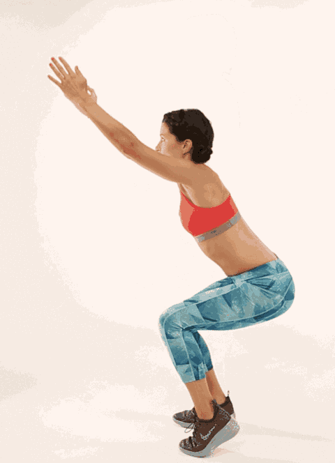a woman in a red sports bra and blue leggings squatting