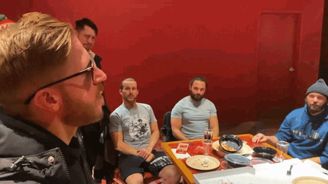 a group of men are sitting around a table with one wearing a shirt that says ' a ' on it