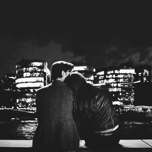 a black and white photo of a man and a woman looking at the city at night