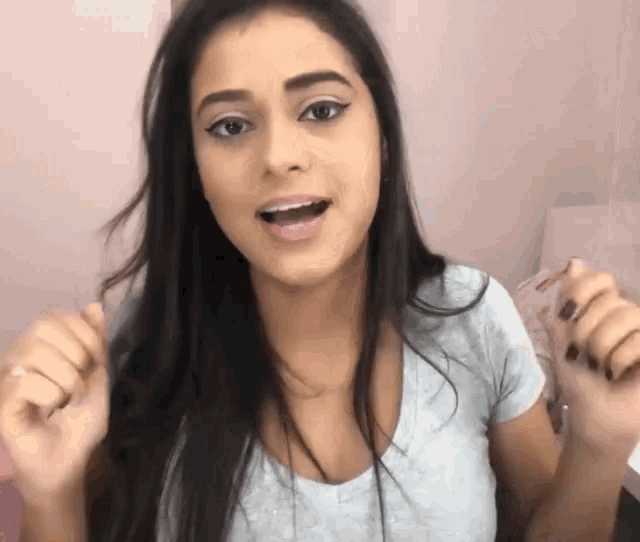 a woman with long dark hair is wearing a white shirt and making a funny face