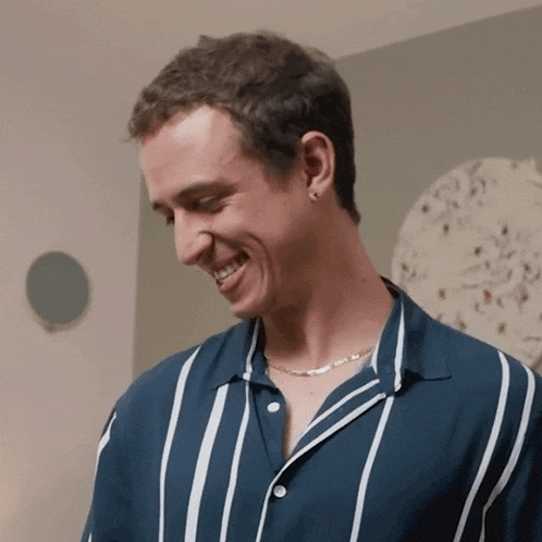 a man wearing a blue and white striped shirt and a necklace smiles