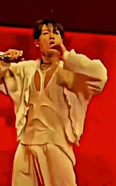 a man in a white shirt and white pants stands in front of a red wall