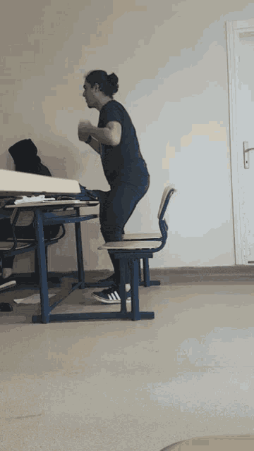 a man squatting on a chair in front of a desk