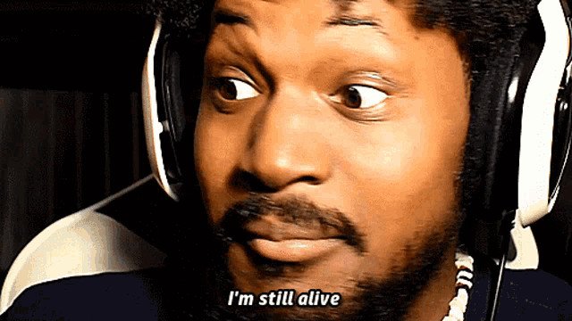 a man wearing headphones and a necklace says i 'm still alive