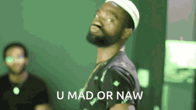 a man with a beard is standing in front of a green background that says u mad or naw