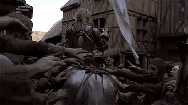 a man in armor is riding on the back of a horse while a crowd of people reach out to touch him .