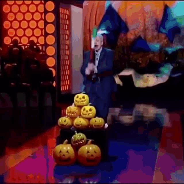 a man in a suit is standing in front of a pile of pumpkins on a stage .