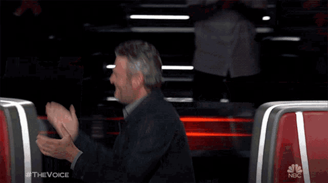a man is laughing while sitting in a chair on a show called the voice