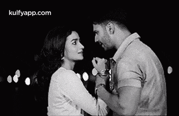 a man and a woman are holding hands and looking at each other .