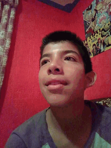a young boy is smiling in front of a red wall with a poster on it that says what