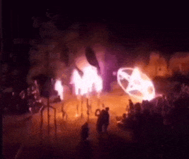 a group of people are standing in front of a fire with a pentagram on it .