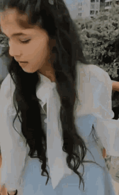 a young girl with long black hair is wearing a white shirt and a blue dress .