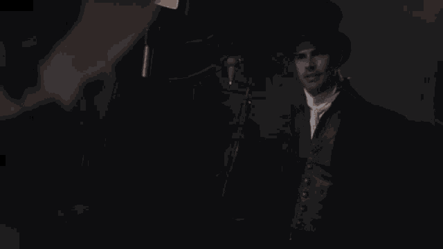a man in a top hat and suit stands in a dark room