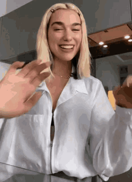 a woman in a white shirt is smiling and waving