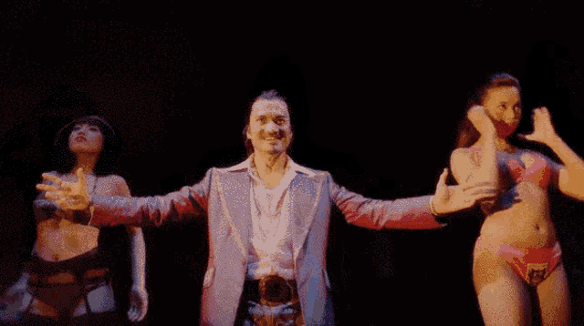 a man with his arms outstretched is surrounded by two women in bikinis