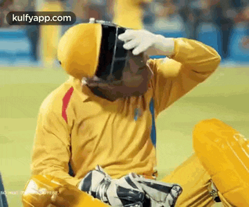 a man wearing a yellow shirt and gloves is sitting on a cricket field .