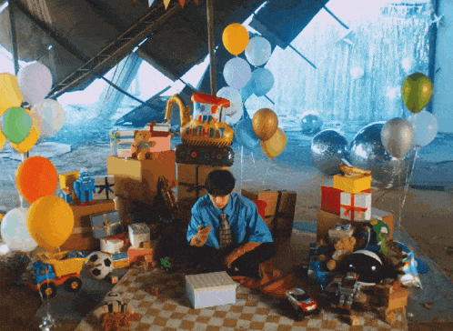 a boy sits in a room surrounded by balloons and toys