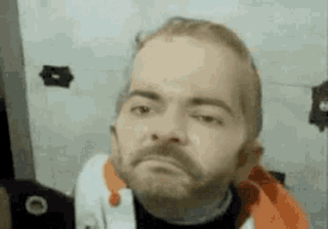 a man with a beard is looking at the camera with a serious look on his face .