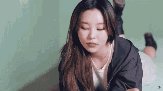 a woman in a black jacket is laying on her stomach with her eyes closed .