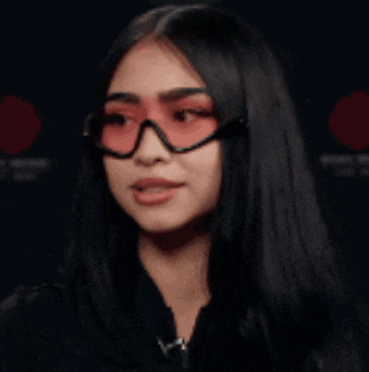 a woman wearing red glasses and a black jacket is making a funny face .