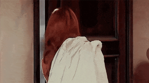 a woman with red hair is standing in front of a door wearing a white hooded robe .