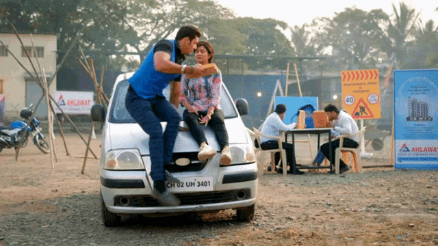 a man and a woman are sitting on the hood of a white car with a license plate that says ch 02 um 3401