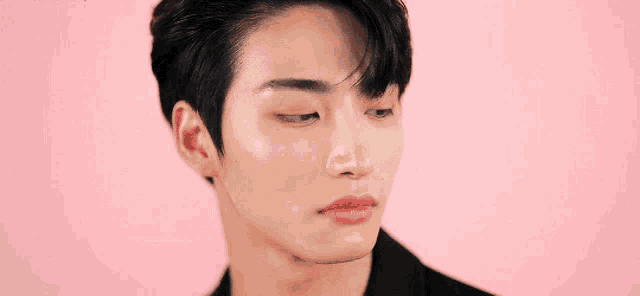 a close up of a young man 's face with a pink background and a black jacket .