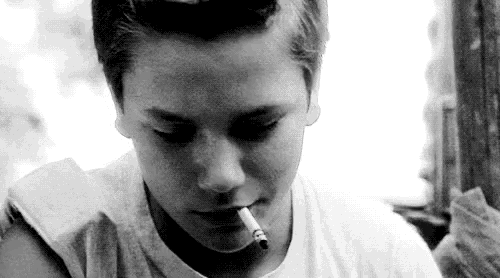 a black and white photo of a boy smoking a cigarette .