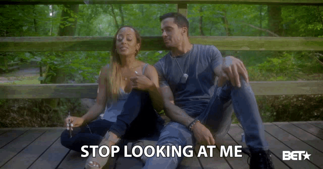 a man and a woman are sitting on a wooden deck with the words stop looking at me above them
