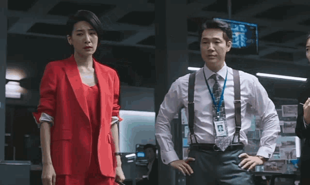 a woman in a red suit stands next to a man in a white shirt and suspenders