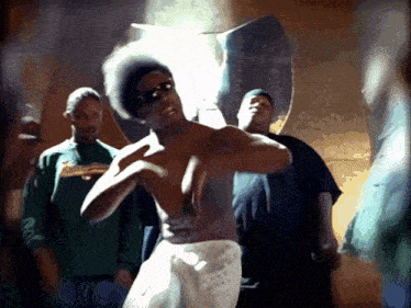 a shirtless man in a white towel is dancing in front of a group of men