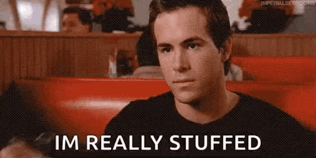 a man is sitting in a diner with the words `` im really stuffed '' written next to him .
