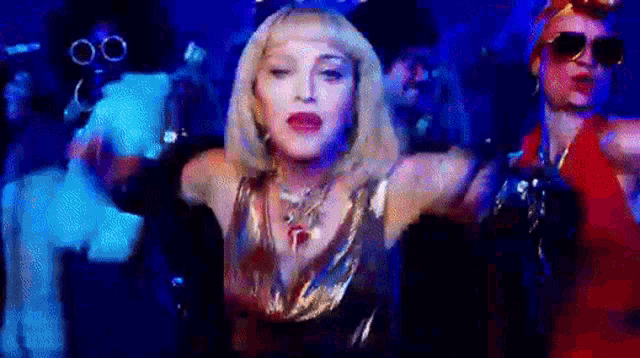 a woman in a gold dress is dancing in front of a group of people in a dark room .