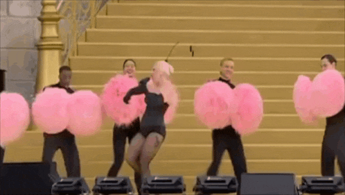 a group of people are standing on a stage holding pink balloons .
