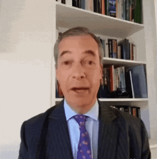 a man in a suit and tie stands in front of a bookcase